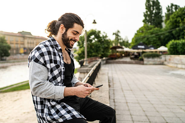istock Young man using smartphone while sitting on riverbank in city 2225966989