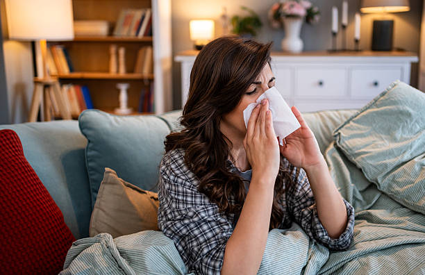 istock Young woman blowing nose while resting on couch at home 2225967036