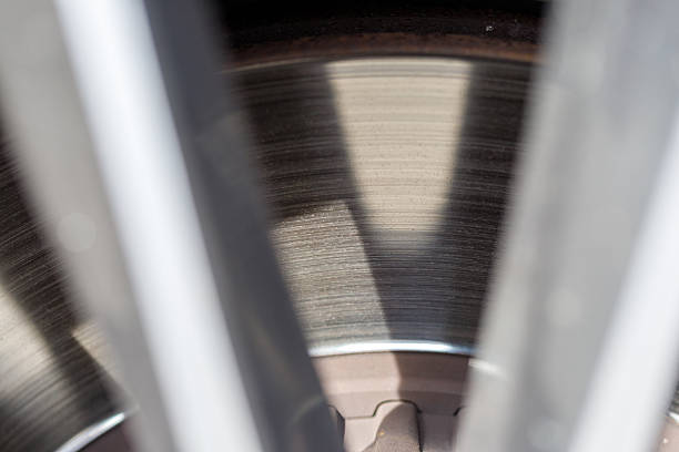 Close-up of a vehicle's disc brake, viewed through the spokes of a wheel. Light and shadow create contrasting patterns.
