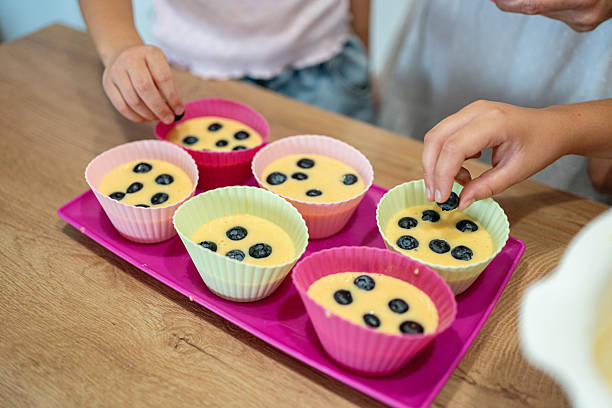 Children preparing homemade blueberry muffins in colorful silicone baking cups