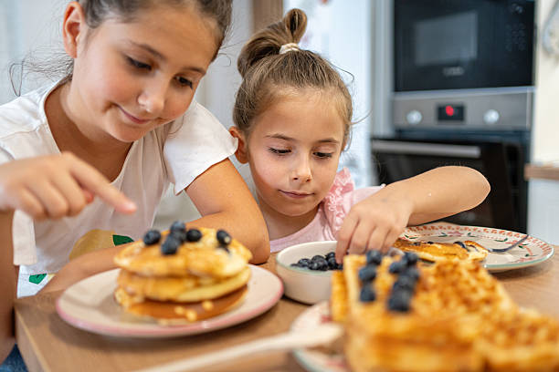 istock Two young children enjoying waffles with blueberries in a home kitchen setting 2225971259