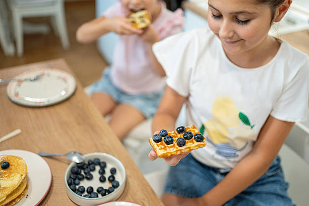Children sharing a delightful breakfast with waffles and fresh blueberries in a cozy home setting.