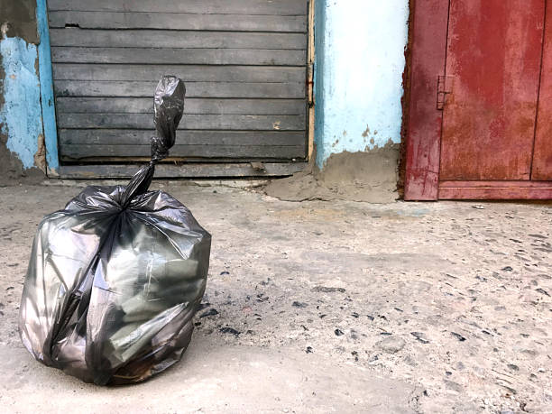 Volunteer Worker showing teenage girls to pick up garbage in their community.  They are holding black rubbish bags and are putting the trash rubbish inside.