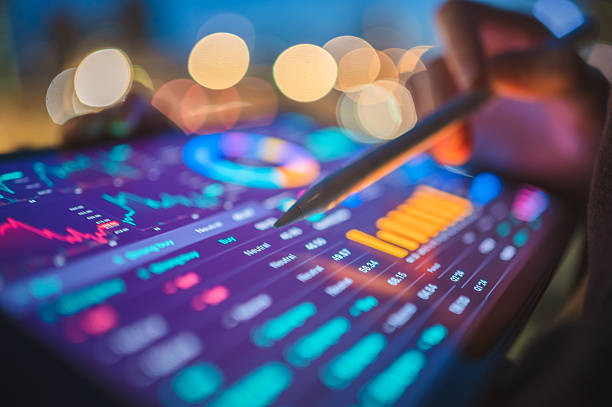 istock Close-up of a hand with a stylus interacting with a vibrant digital tablet displaying glowing financial charts and graphs against a blurred background, representing advanced data analysis. 2225980320