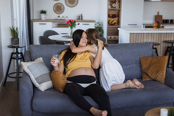 istock Pregnant mother drinking water and hugging daughter on sofa 2225980593