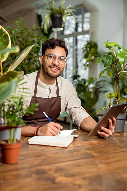 istock Young male shop assistant making notes while working in the flower shop 2225980805