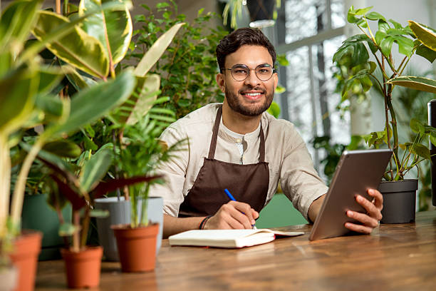 istock Young male shop assistant making notes while working in the flower shop 2225980819