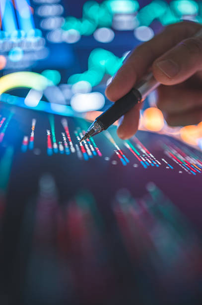 istock A hand operating a stylus on a tablet screen, showing glowing blue and red financial charts links to data security analysis, the development of AI systems for predictive analytics, or secure coding practices within digital environments. 2225981686