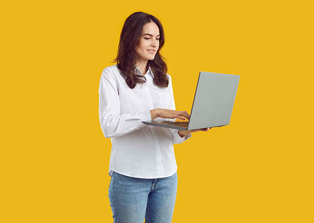 istock Young businesswoman standing isolated on yellow background and using laptop computer 2225982368