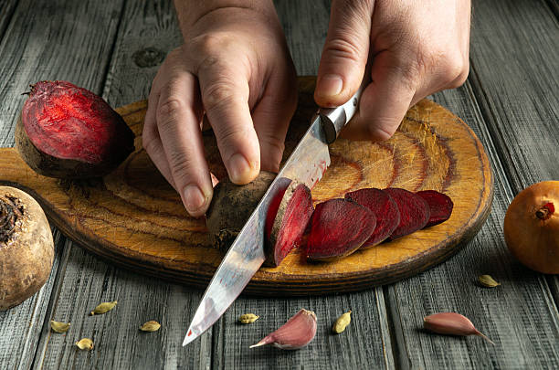 istock A person skillfully slices vibrant red beets with a sharp knife on a wooden cutting board. Surrounding ingredients include garlic and spices, creating a cozy cooking atmosphere 2225982455