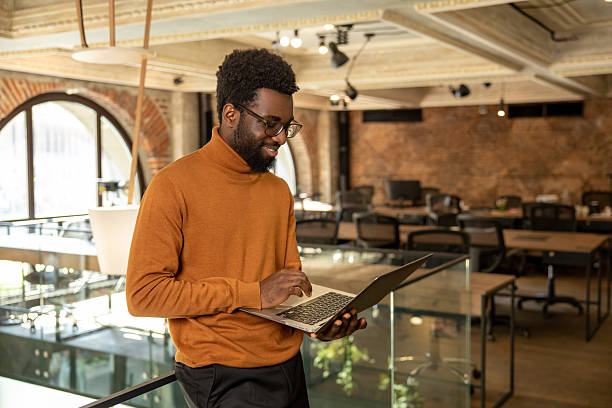 istock Smiling diverse entrepreneur holding computer and standing near railing in office 2225991362