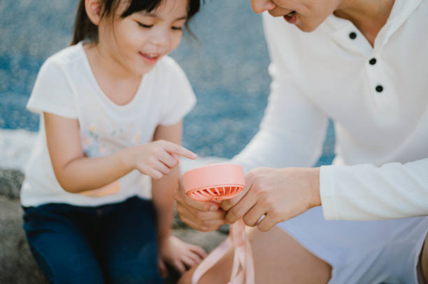 istock Curious Asian Girl Pointing at Handheld Fan Held by Her Father 2225992383