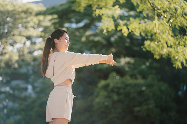 Asian woman stretching in a quiet green space during a morning workout, representing wellness, body awareness, and the joy of exercising in a serene environment.