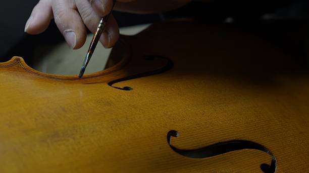 istock Skilled craftsman applying varnish to violin using brush and fingertip, highlighting meticulous woodworking technique during delicate instrument antiquing process 2225994902