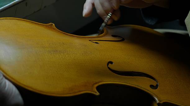 istock Skilled luthier brushing golden varnish along violin soundboard, carefully layering protective finish with precise, delicate strokes 2225994938
