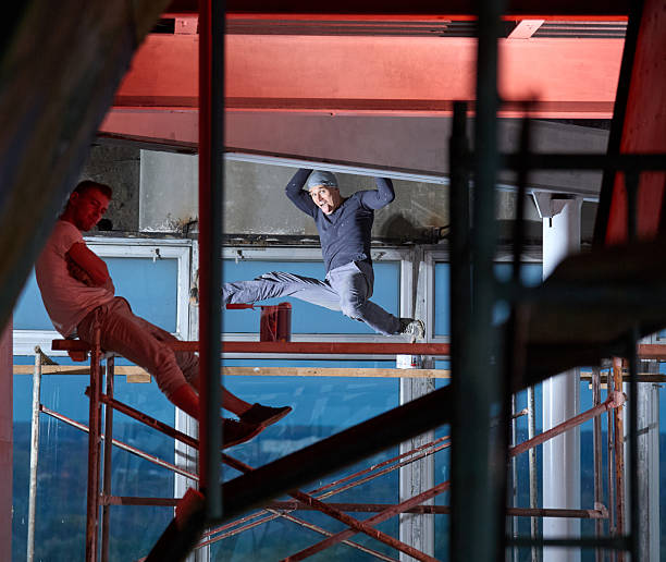 Two cheerful construction workers are working on the scaffolding assembling a sport climbing structure