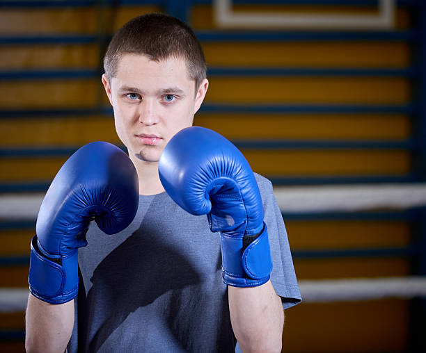 Teenage boy holds his hands in boxing gloves in a boxing stance. Shooting in a gym