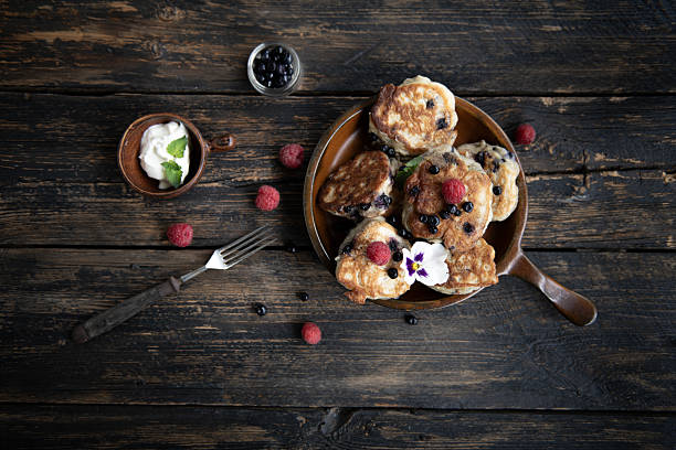 Stack of homemade pancakes with whipped cream, fresh raspberries, and edible flowers. Rustic slow breakfast in dark vintage food photography style