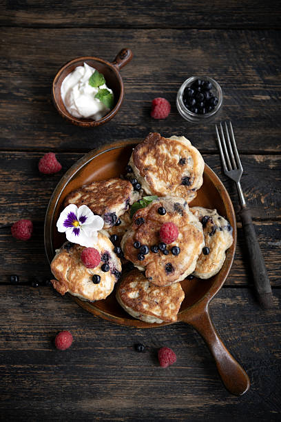 Delicious stack of homemade pancakes with raspberries and cream served on rustic plate. Dark moody food photography.