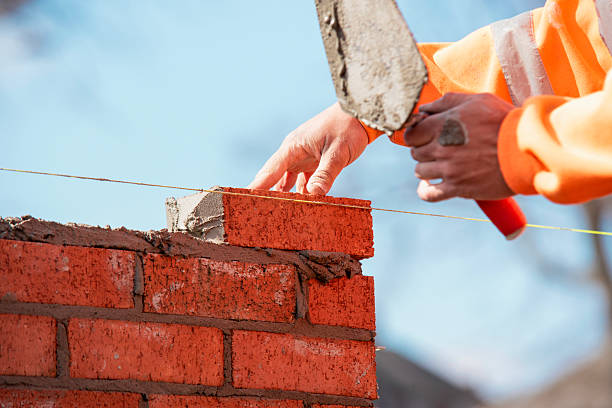 istock Close-up of skilled bricklayer working on construction site laying one more red brickin the wall 2226003412