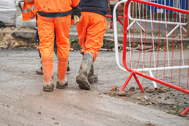 istock Two construction workers in high visibility jackets stroll along a muddy site, surrounded by equipment and safety barriers 2226004743