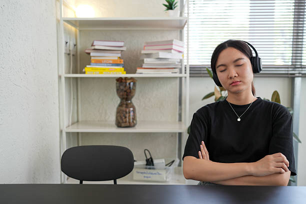 phụ nữ trẻ châu á thư giãn trên chiếc ghế ấm cúng, đeo tai nghe over-ear và vòng cổ ai công nghệ cao, điều khiển âm nhạc rảnh tay - tai nghe overear hình ảnh sẵn có, bức ảnh & hình ảnh trả phí bản quyền một lần