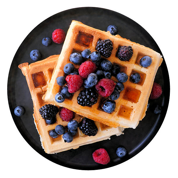 Breakfast waffles with raspberries, blueberries and blackberries on a black plate. Above view isolated on a white background.