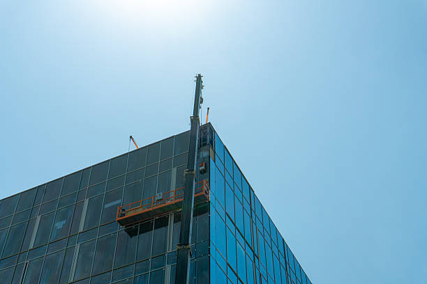 istock Contemporary high rise structure featuring reflective glass facade, construction workers on suspended platform, visible cranes, steel beams, illustrating urban development and architectural progress 2226010960