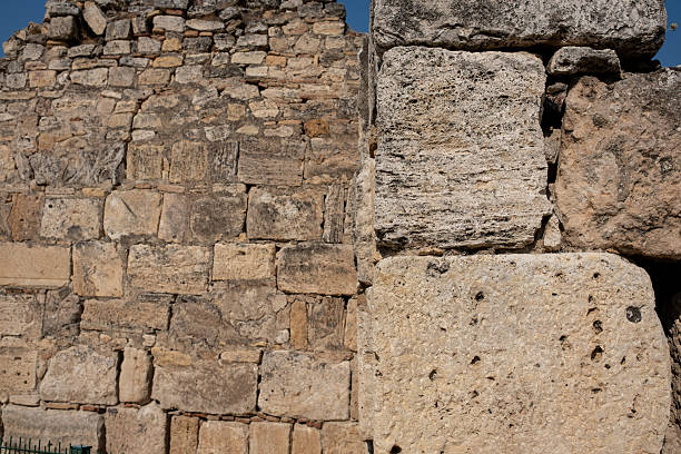 Visitors admire the ancient stone walls of Pamukkale, highlighting the intricate patterns and textures under the warm sun.