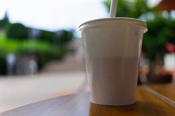 A plain, disposable drink cup with a lid and straw sits on a wooden outdoor table, ideal for showcasing logo or branding mockups in a casual, real-life setting.
