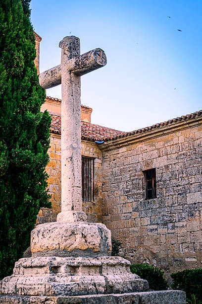Ancient stone cross located in Ampudia, Palencia (Spain), standing beside historic buildings and bathed in warm afternoon light.