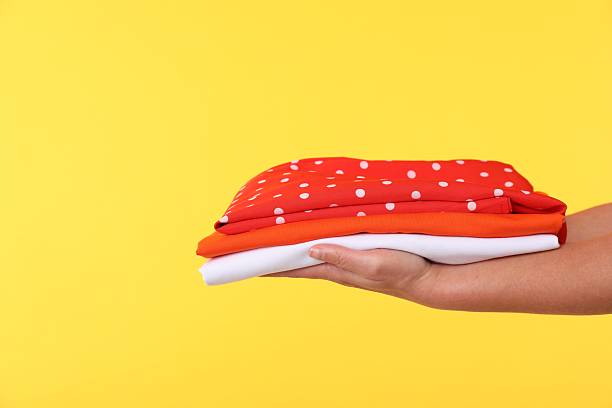 Woman holding stack of clothes on yellow background, closeup. Space for text