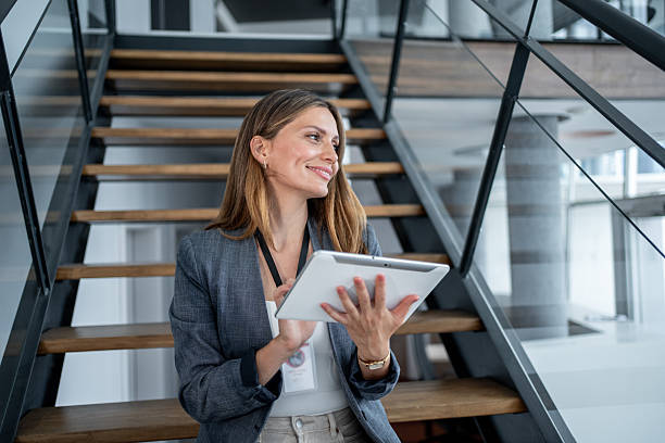 istock Businesswoman smiling and using digital tablet on stairs in modern office 2226038937