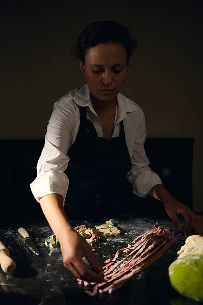 Female chef makes pasta with Italian flag-inspired colors, showcasing traditional cooking in ambient lighting. Perfect depiction of culinary art and Italian gastronomy.