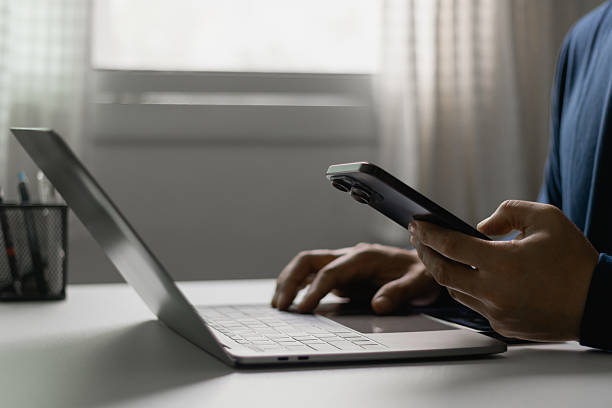 istock Businessman working with smartphone and laptop, digital communication, multitasking, online business concept. Man scroll social media, checks email, manages business processes, remote work from home. 2226043508