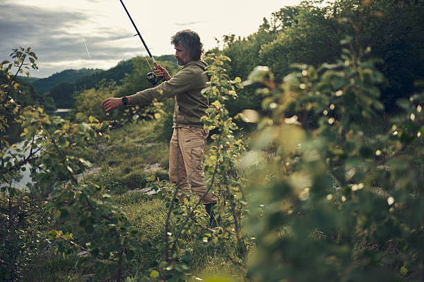 Saint-Petersburg, Russia. A person with fishing rods is fishing on the bank of a reservoir surrounded by green grass and trees.