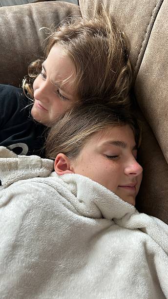 Two young sisters enjoying a quiet moment snuggled up on the couch on a rainy afternoon.