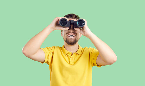 istock Happy young traveller isolated on green background looking through binoculars and smiling 2226056006