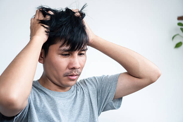 Asian Man Sitting Alone Indoors on a Couch, Holding His Head