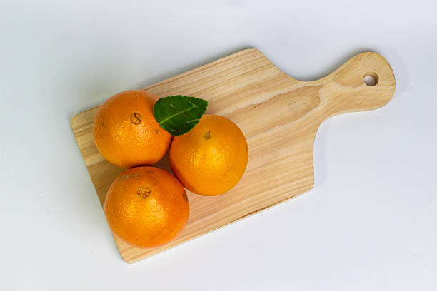 istock Three Fresh Tangerines on Wooden Cutting Board A Vibrant Citrus Fruit Composition featuring Ripe Oranges with Green Leaf on Light Wood Surface Isolated on White for Stock Photography 2226091331