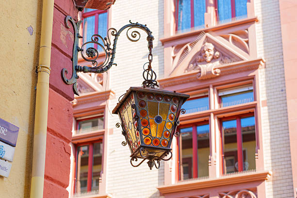Vibrant, ornate lantern hangs from a historic building in Heidelberg, showcasing intricate designs and colorful glass elements against the backdrop of classic architecture.
