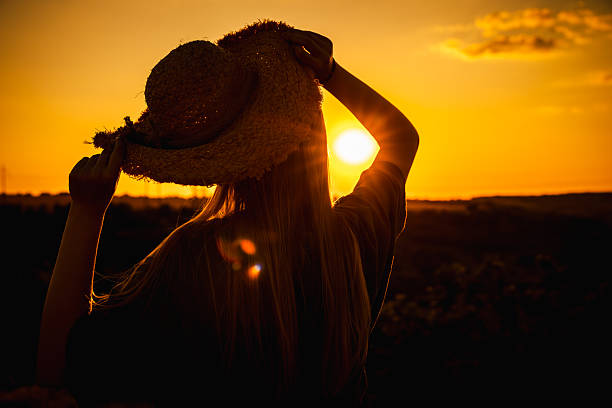 istock Young woman in silhouette holding a straw hat while watching the sunset over a rural landscape, with golden light and peaceful atmosphere 2226094326