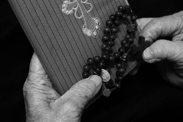 The Divine Mercy devotion concept with a prayer hand holding The Divine Mercy rosary beads with the holy heart of Jesus Christ, the Catholic symbol on black and white background.