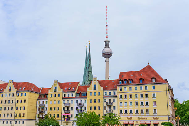Berlin, Germany - June 1, 2025: Historic buildings with red roofs and a prominent television tower against a cloudy sky in Berlin, Germany, showcasing the city's architectural blend.