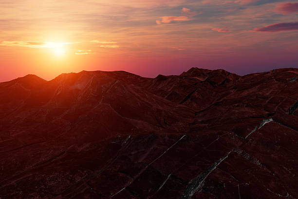 A mountain range with a sunset in the background. The sun is setting behind the mountains. The sky is orange and pink