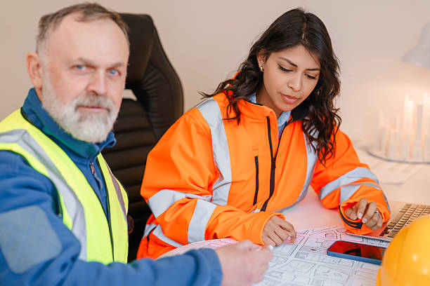 istock Female structural engineer collaborating with male project manager on construction plans in office with safety gear and technology around 2226112117