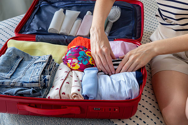 istock A woman packing clothes into a suitcase for a summer vacation while sitting on a bed in a bedroom. Getting ready for a vacation. Open suitcase overflowing with clothes 2226114579