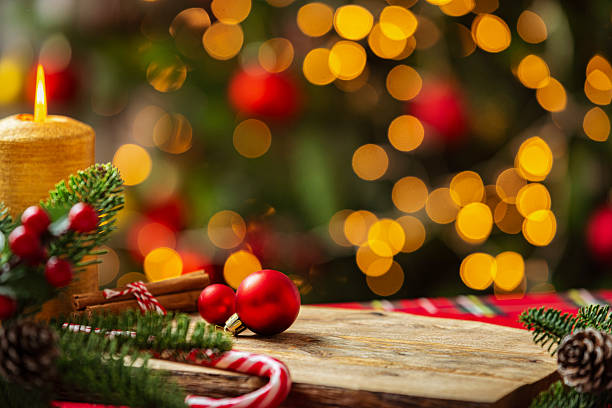 Cozy Christmas decoration with burning candle, pine branches and defocused Christmas tree at background. Ideal for product montage or copy space. Christmas ornament and candy cane