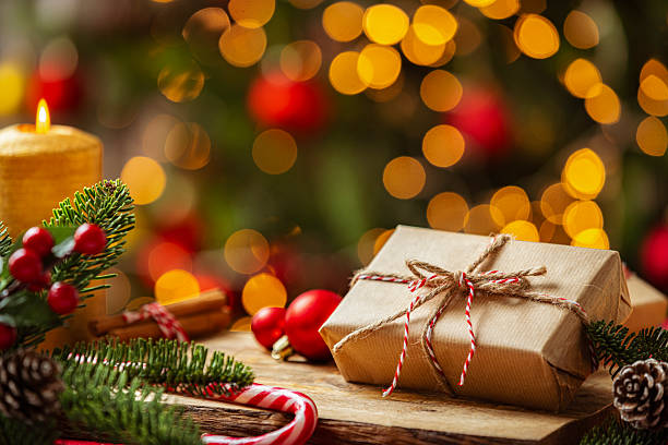 istock Christmas present on a cozy table with defocused Christmas tree at background. Wrapped box, gift and decor with spotted lights. Candy cane or burning candle 2226116654