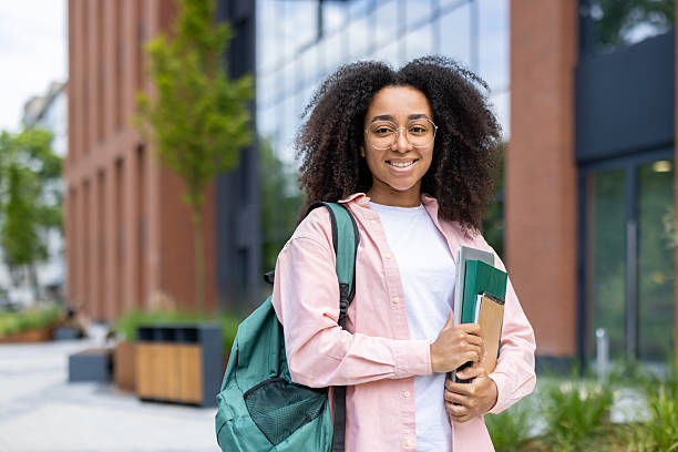 istock A smiling young student, holding books and a backpack, stands outside a university building. 2226117593